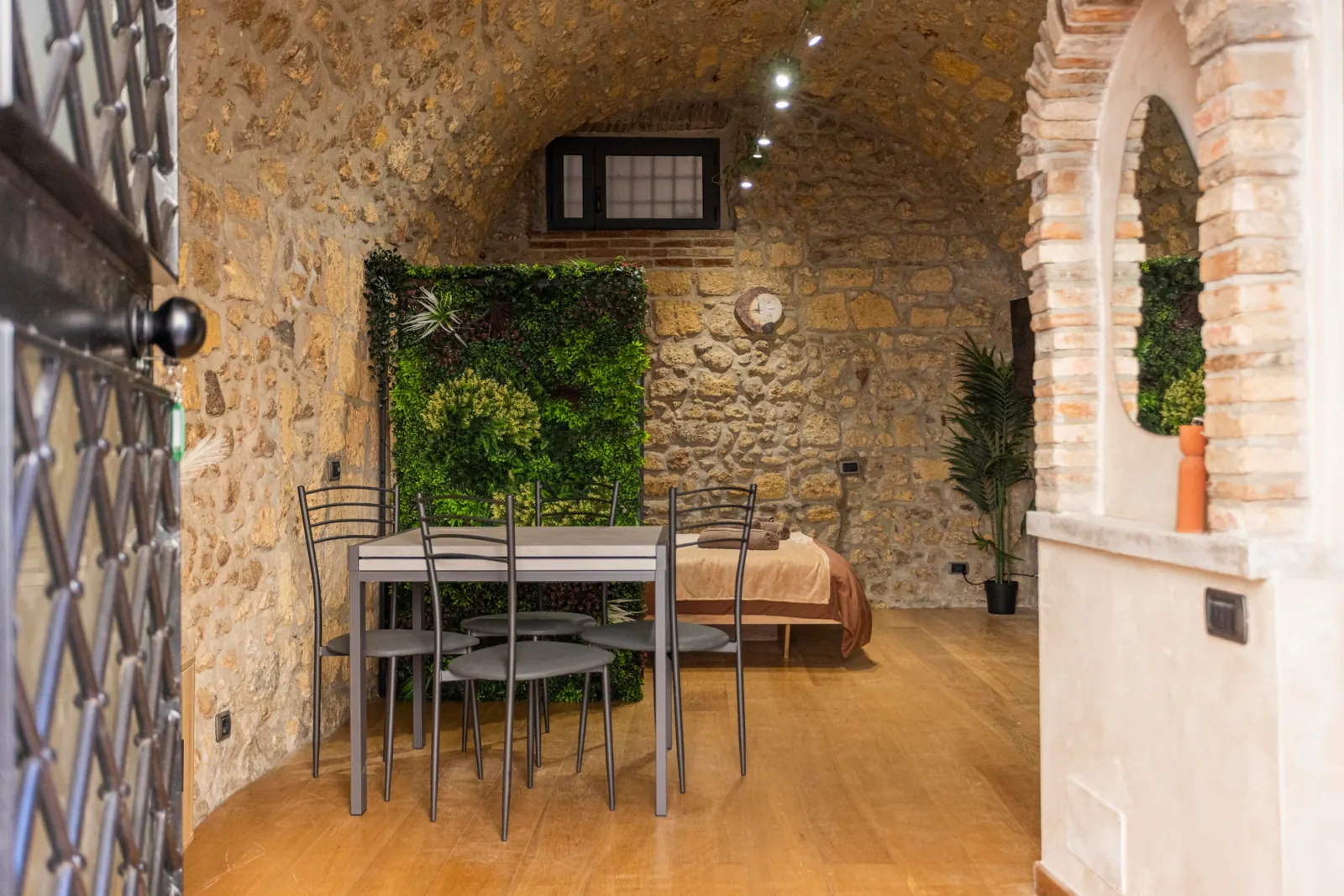 Interno del loft etrusco: volta in pietra, parete di verde, tavolo con quattro sedie e arco in mattoni